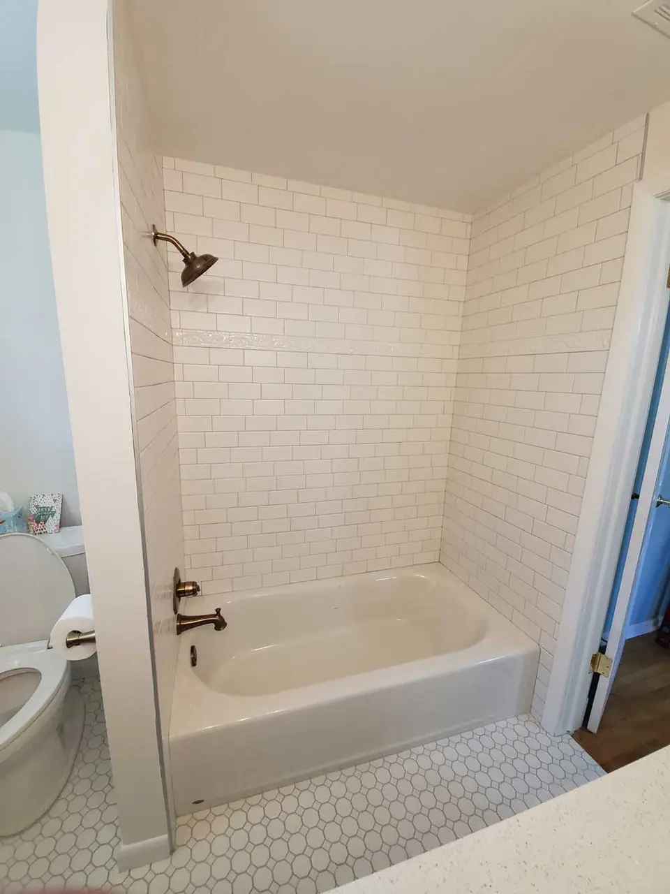 Finished tub surround in white subway tile with a hex mosaic floor